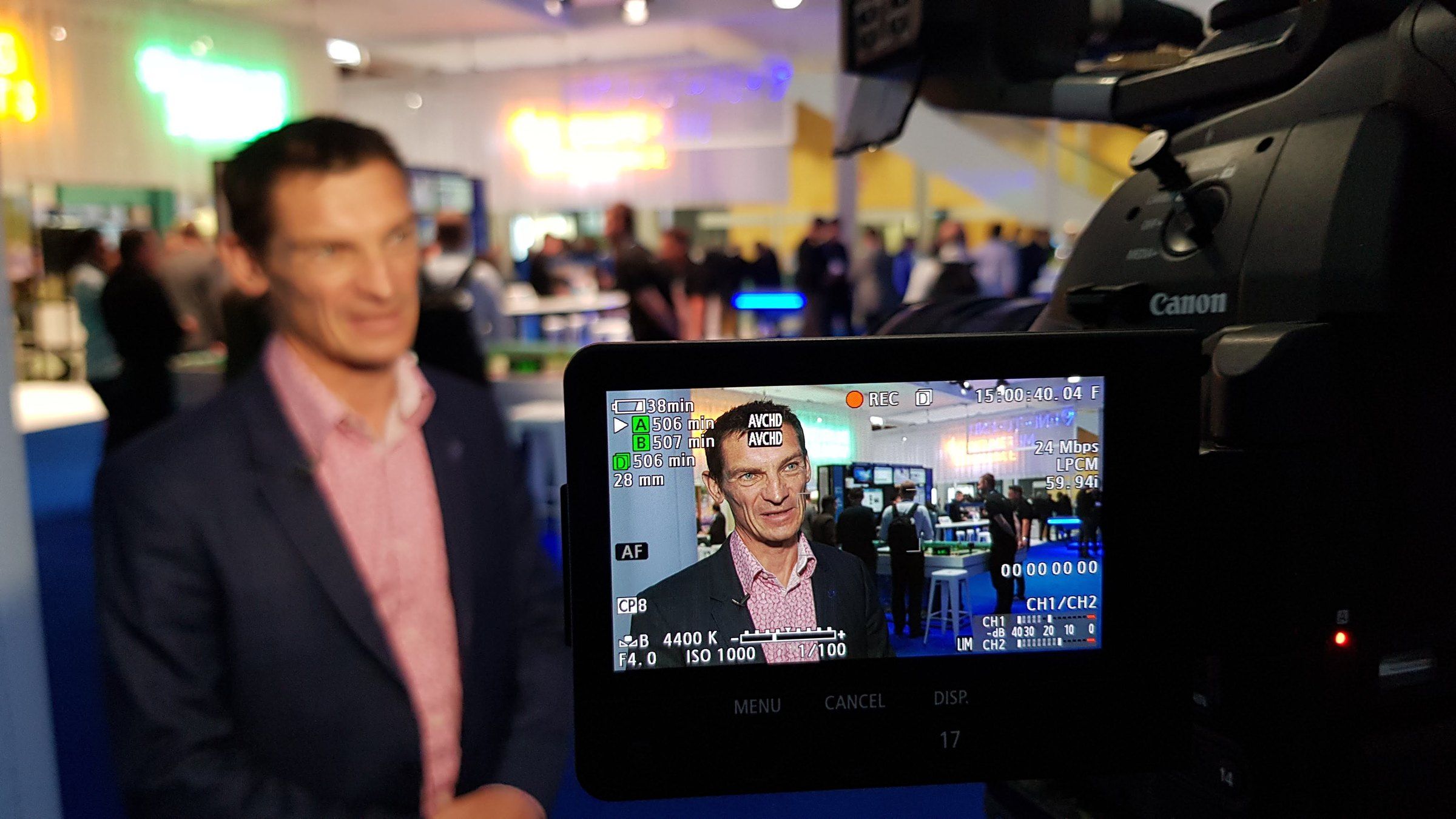 A camera monitor framing an interview on a busy show floor