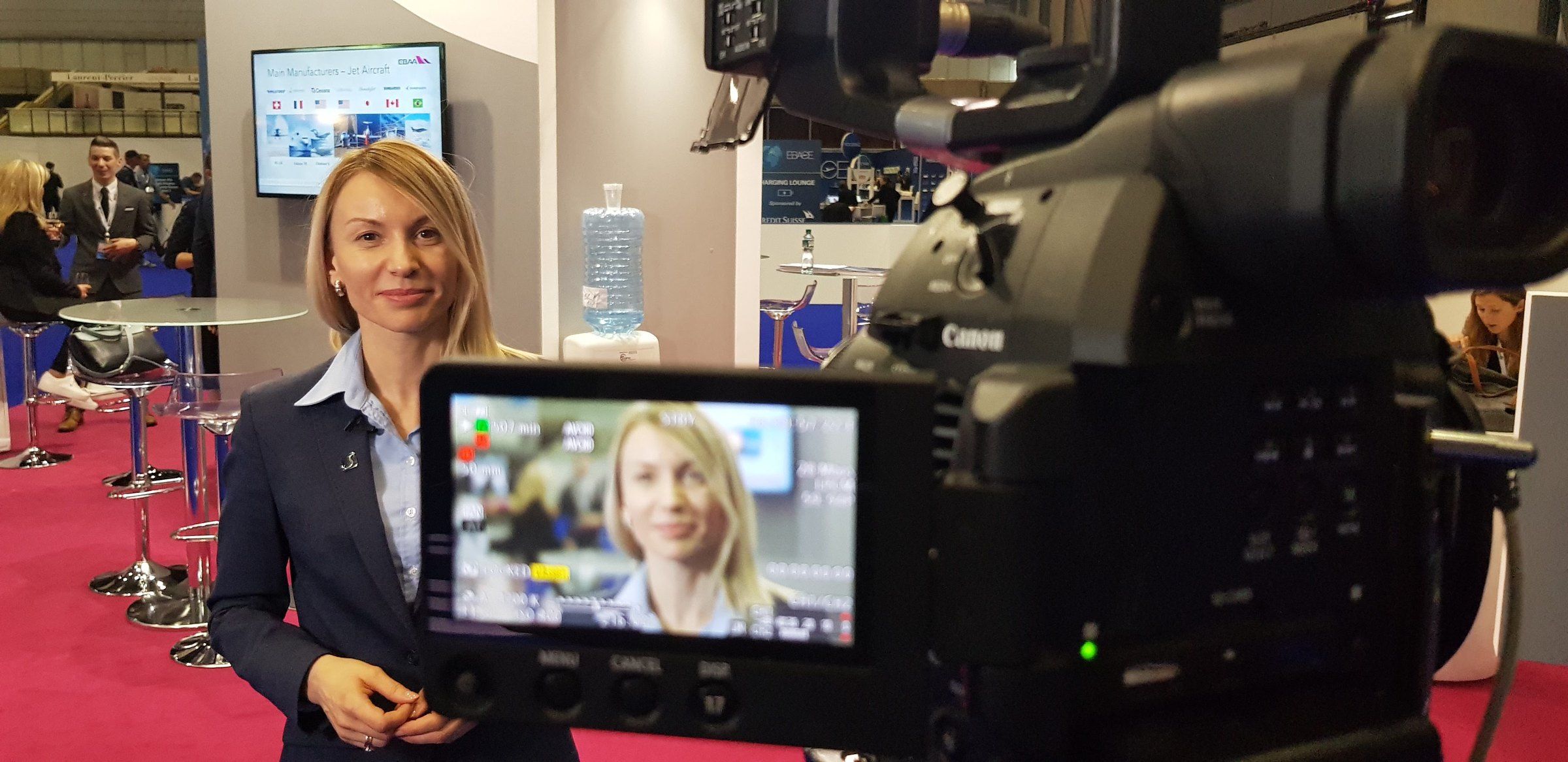 An exhibitor being interviewed on her stand, seen on the camera's monitor