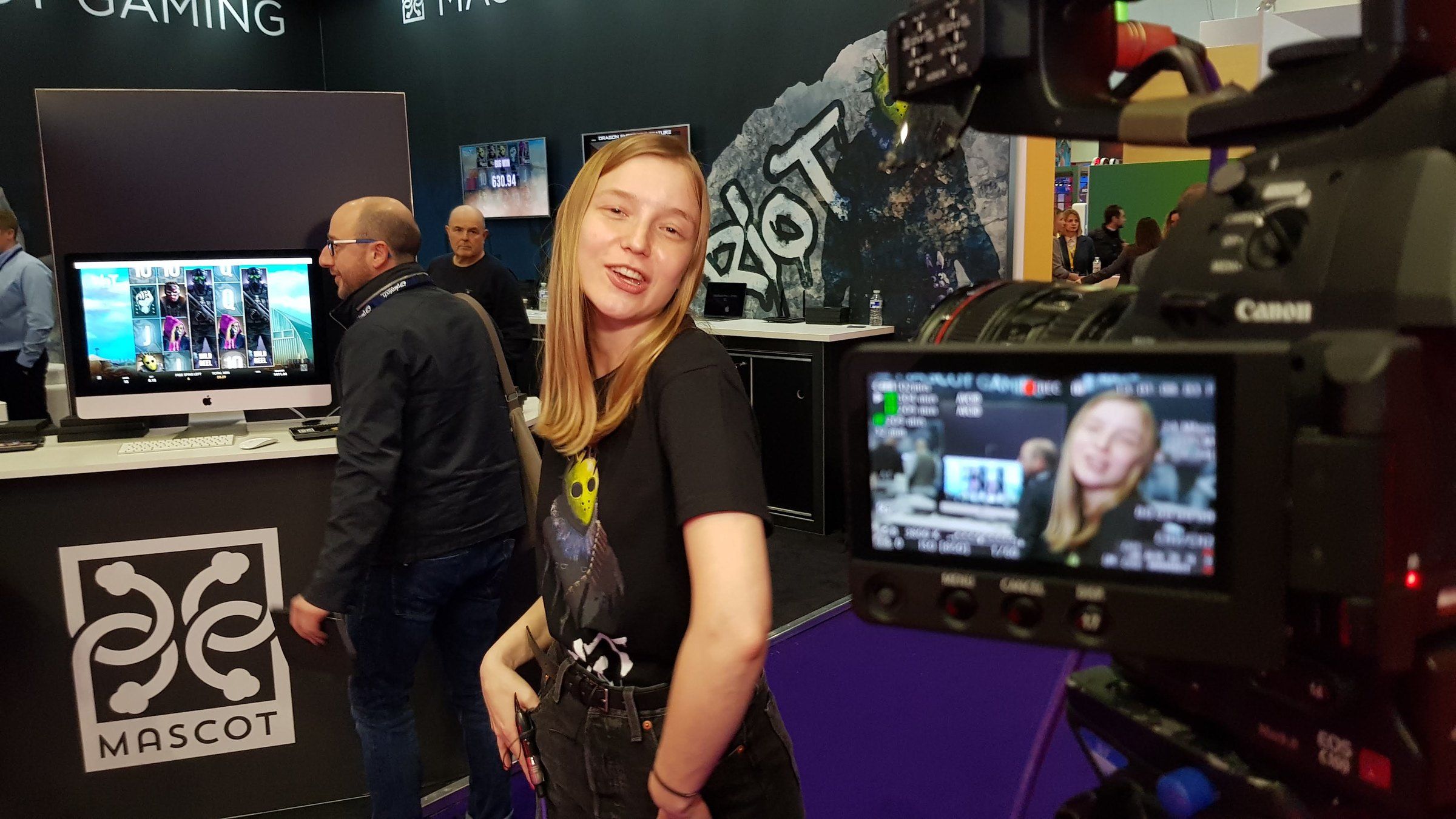 An exhibitor smiling on camera at her stand, shown on the camera monitor